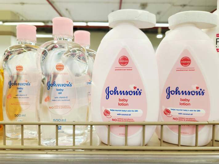 Close-up of a hand applying lavender-vanilla scented lotion into soft, glowing skin; pastel-toned bathroom background with minimalist skincare products